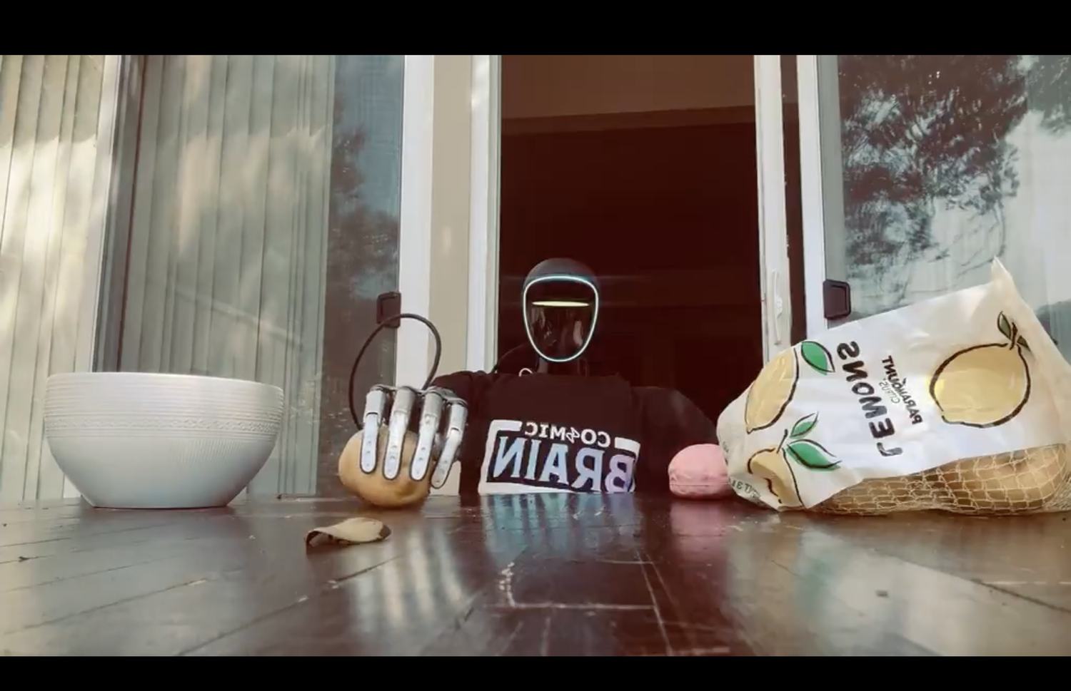 The same robot with its dexterous hand closed around a lemon, lifting it from the deck.